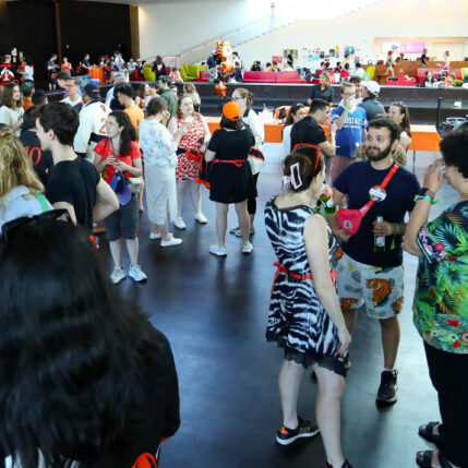 Groups of people stand together in a large crowd in an open indoor space.