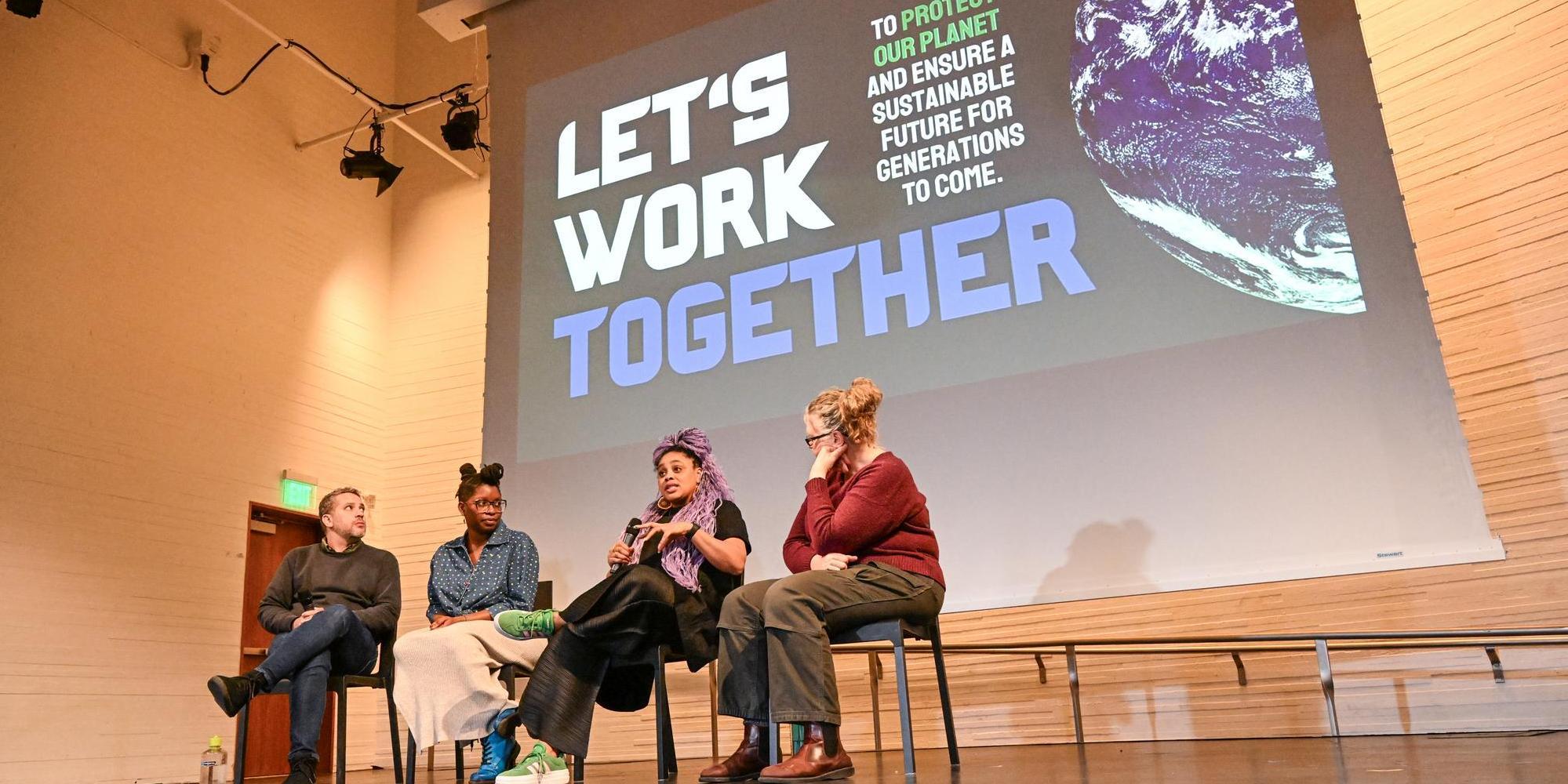 Four people sit onstage talking below a projection screen that says "Let's Work Together" to protect our planet.