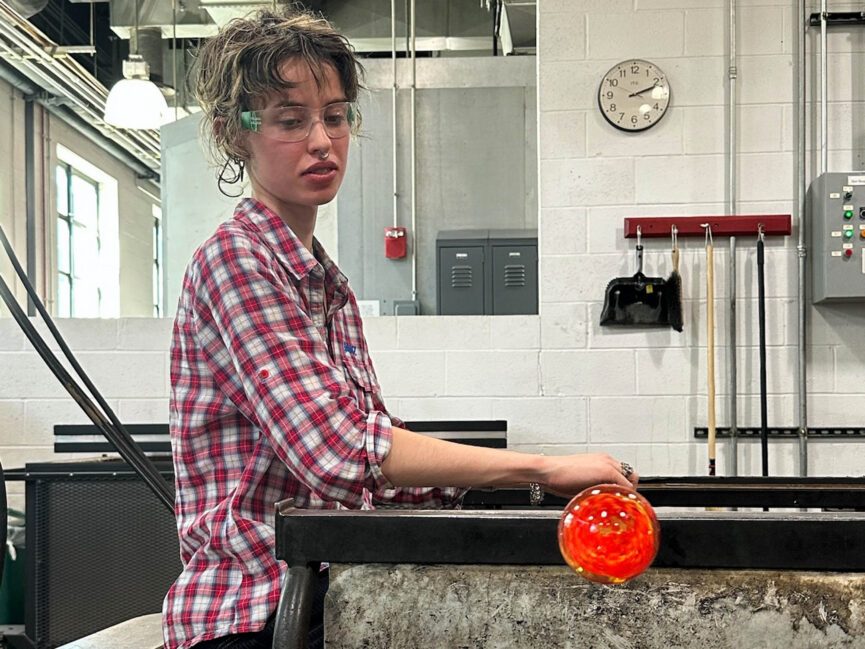 Someone works with hot glass in an industrial setting.