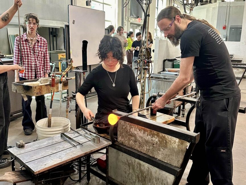 Two people participate in working with glowing hot glass.
