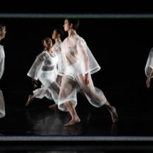 A group of dancers in sheer white costumes dancer onstage.