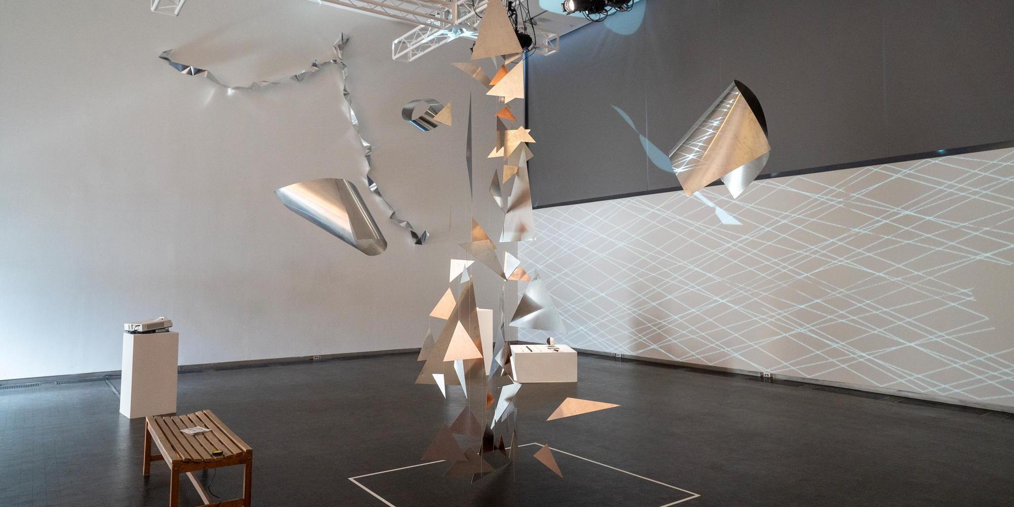 Interior of a gallery space with a silver abstract sculpture hanging from the ceiling