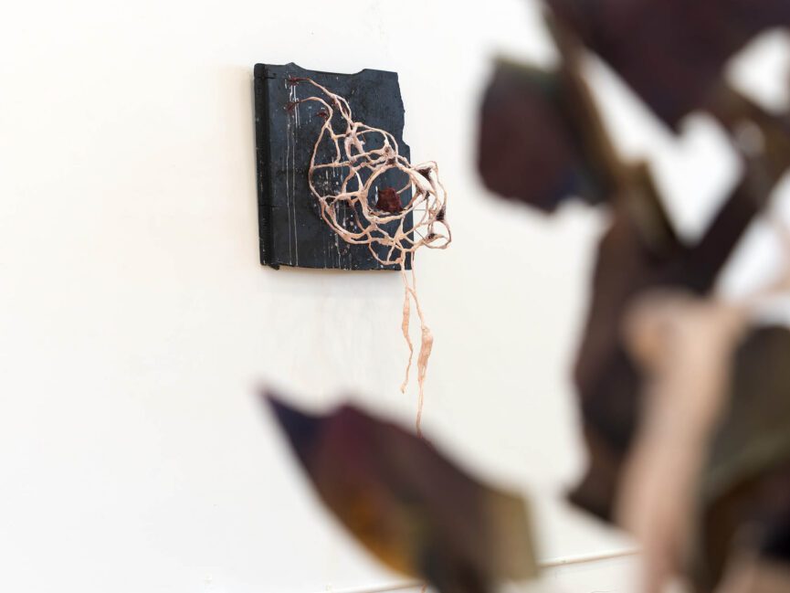 An abstract sculpture hangs on a wall obscured by an object in the foreground.