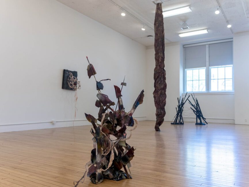 A series of sculptures are on view in a gallery space lit by windows in the background.