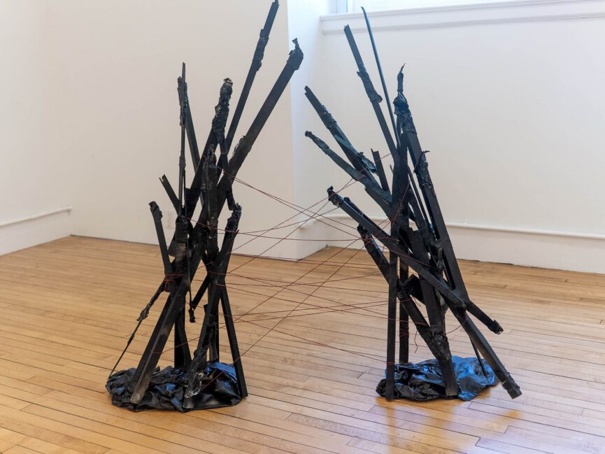 Two similar abstract sculptures are connected by string on the floor of a gallery.