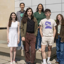 A group of people stand for a portrait outside of a building in front of a reflecting pool.