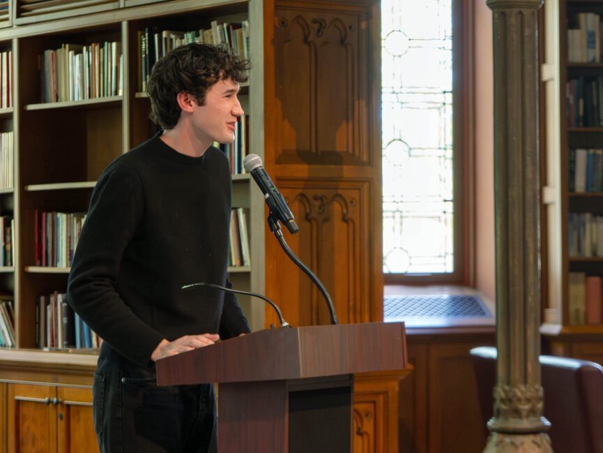 A person reads into a microphone at a podium.