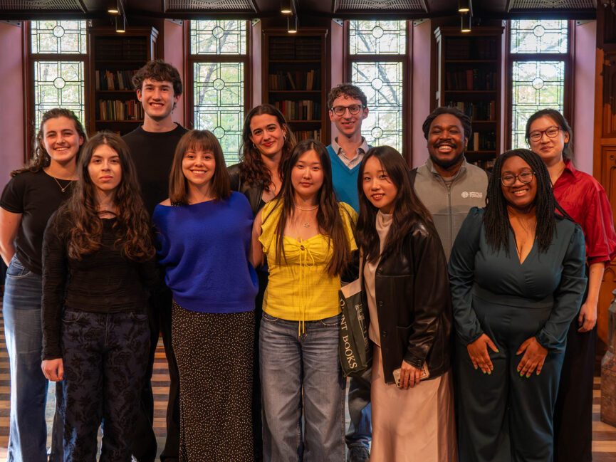 A group of students pose for a photo in front of windows,