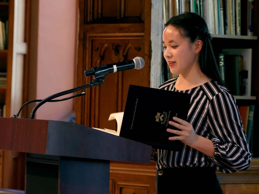 A person reads into a microphone from a folder at a podium.