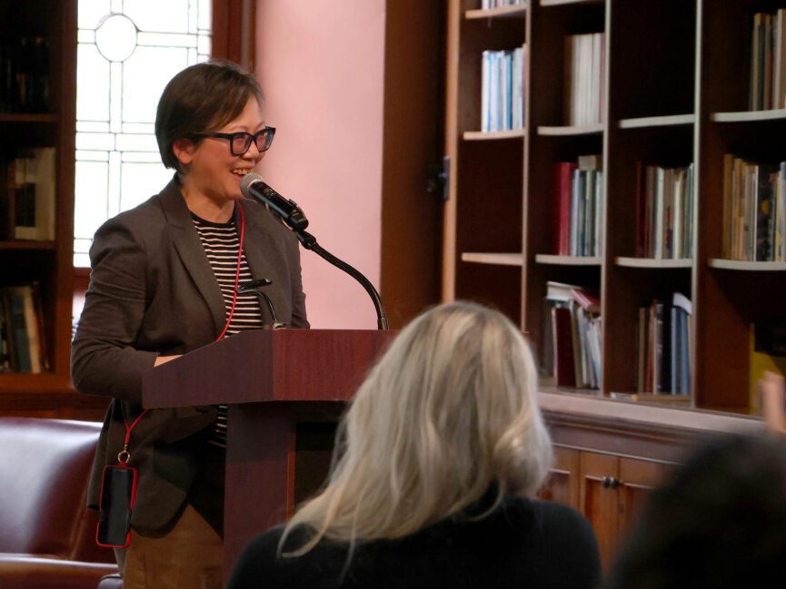 A person reads into a microphone at a podium.