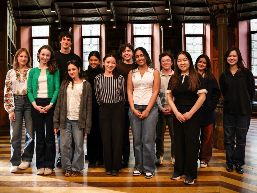 A group of students pose for a photo in front of windows,