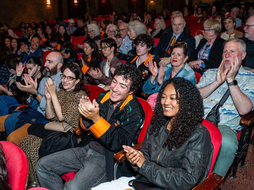 A crowd of people applaud in an auditorium.