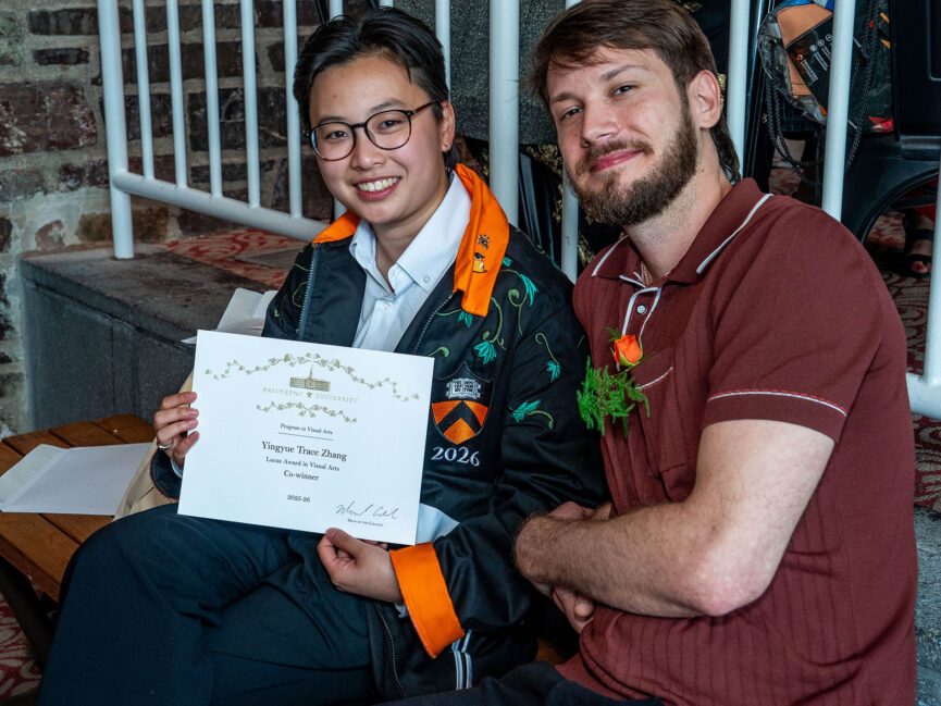 A person holds a piece of paper sitting down next to someone else.